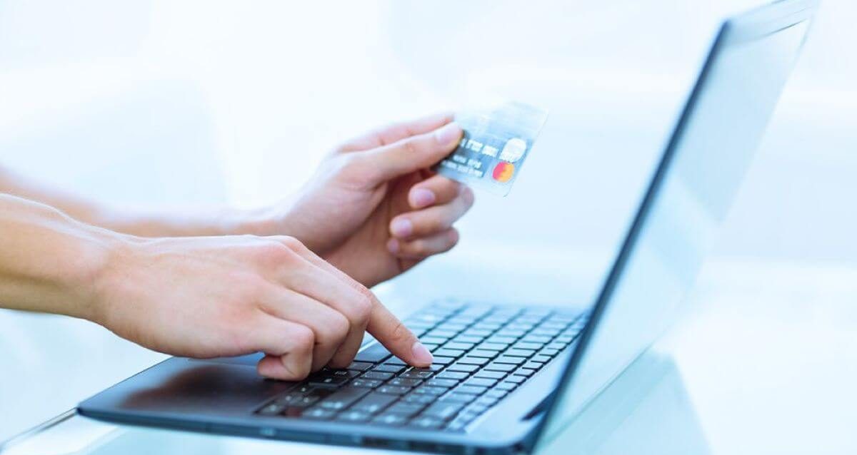 Immagine di una persona che tiene in mano una carta di credito e digita su un computer portatile per eseguire un pagamento anticipato online